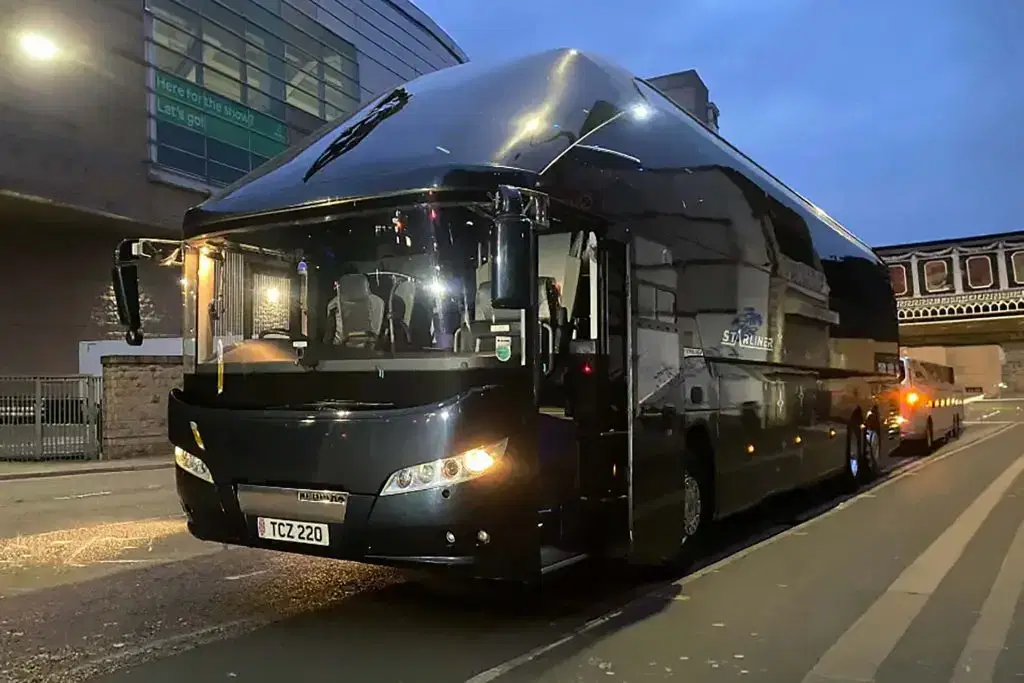 A flagship Tranzcare luxury coach parked outside a major UK music and live performance venue for artist crew tour logistics.