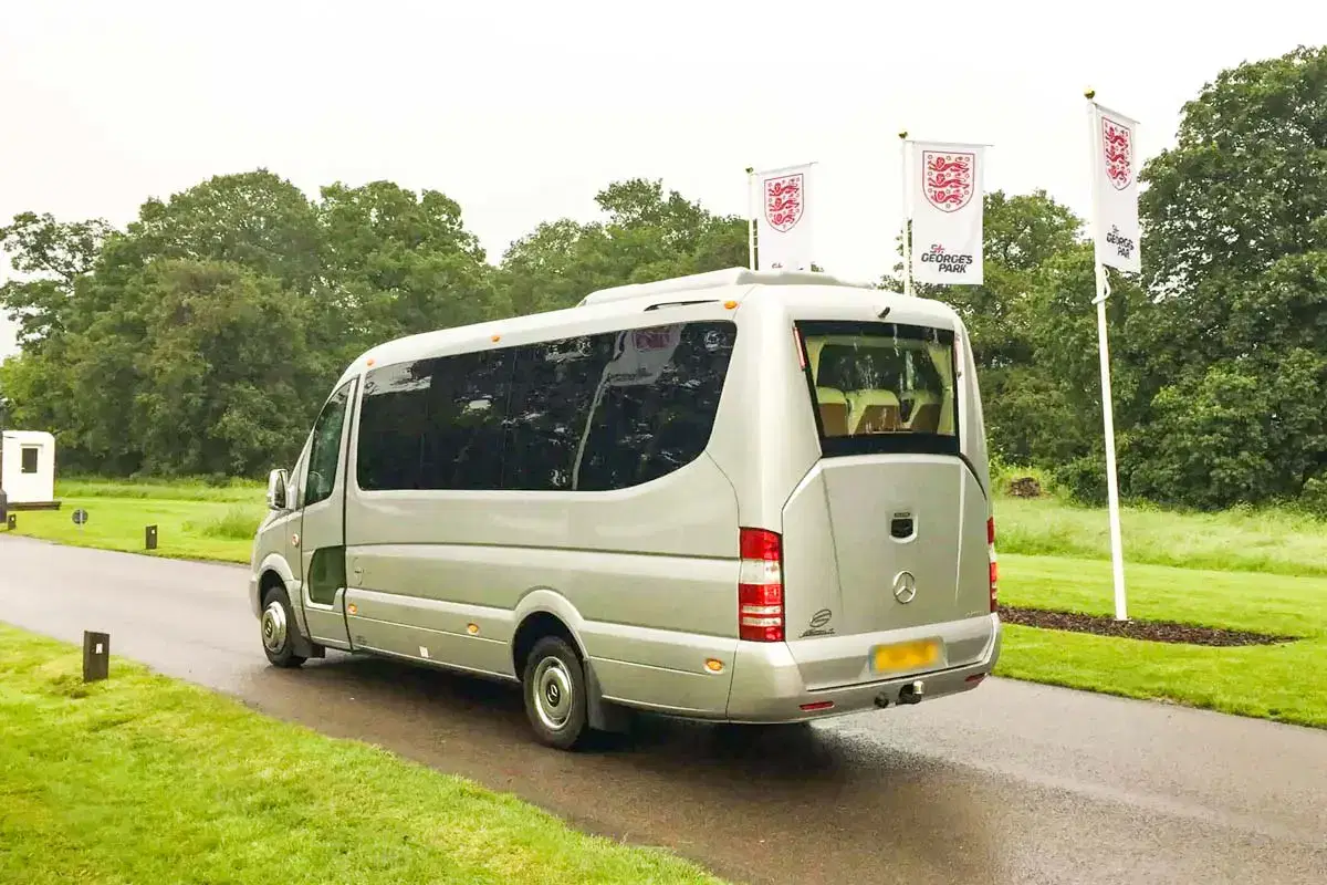 Exterior profile of a modern Tranzcare white executive midi coach parked outside a corporate venue in Manchester.
